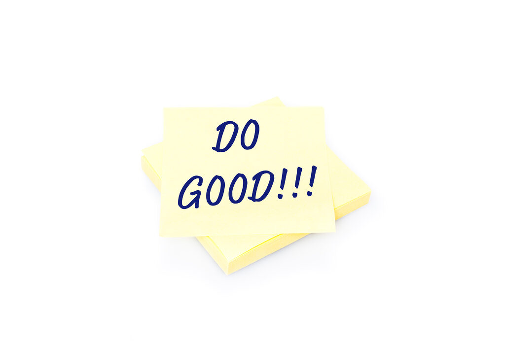 Blank yellow sticky note on block with handwritten message Do Good. Shadow and reflection on white background